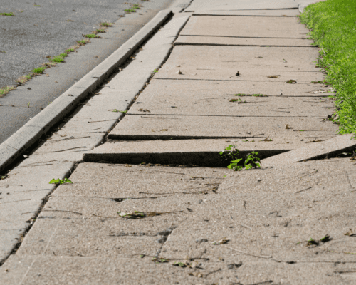 An unkept public side walk with cracks and weeds