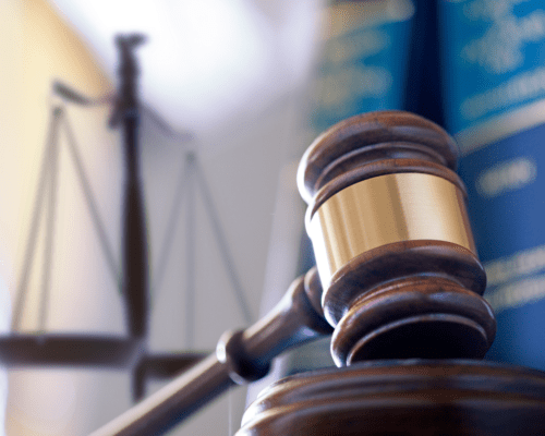 Close-up of a wooden gavel with a brass band resting on a judge’s block, with legal books and scales of justice blurred in the background. The image represents commercial real estate litigation in Los Angeles, emphasizing property rights, CEQA disputes, and legal defense in complex property cases.