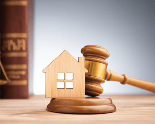 Wooden house model positioned in front of a judge’s gavel, symbolizing real estate law, property rights, and legal proceedings related to title disputes and public acquisitions.